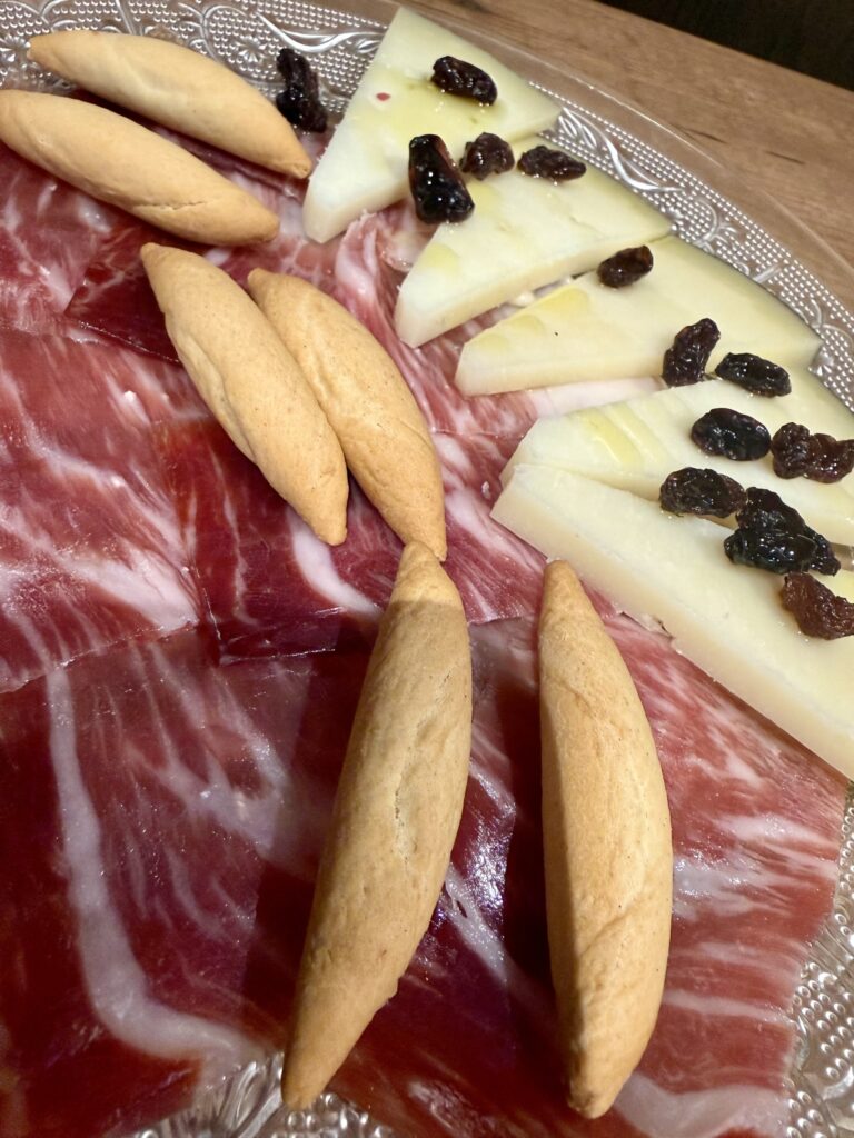 Plato de jamón ibérico con queso, acompañado de panecillos y pasas.
