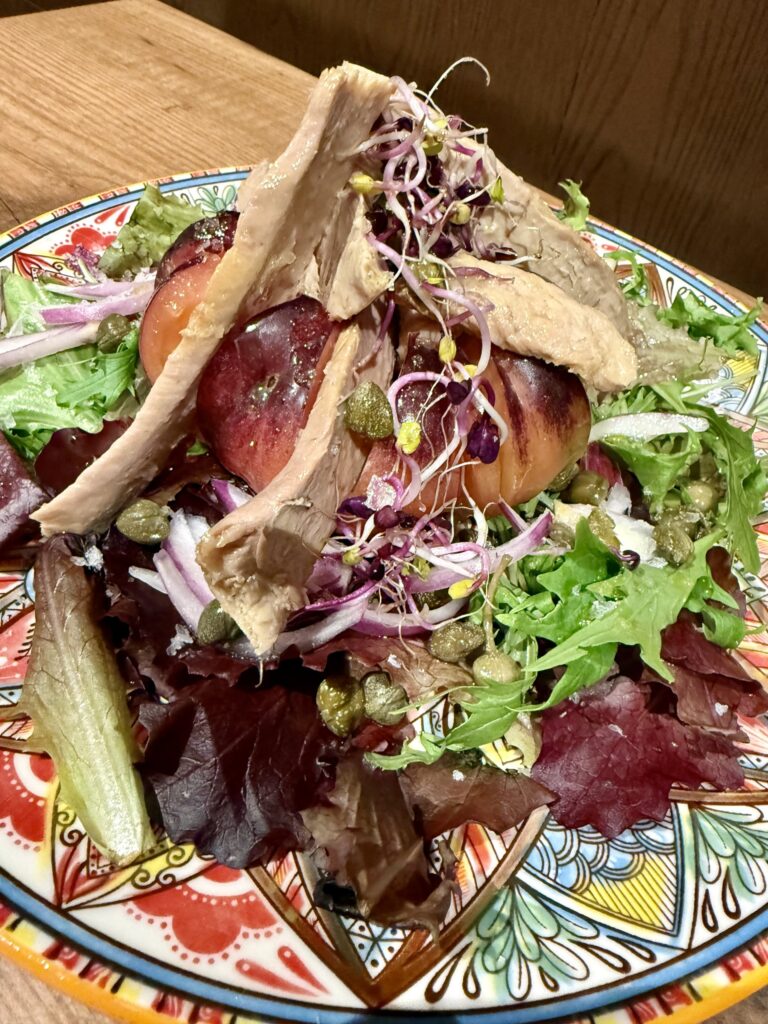Ensalada de tomate valenciano con ventresca, cebolla roja, alcaparras y brotes, servida en un plato colorido.