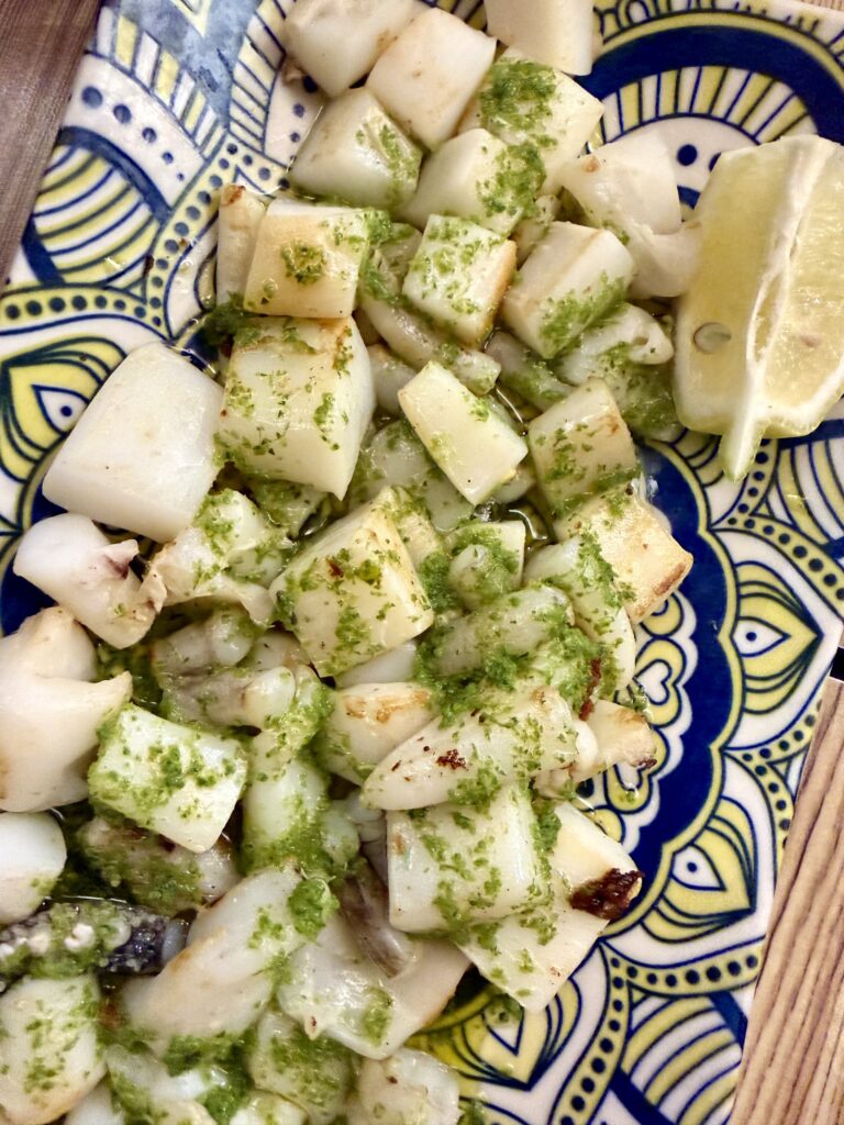 Calamares a la plancha con salsa verde y limón, servidos en un plato colorido.