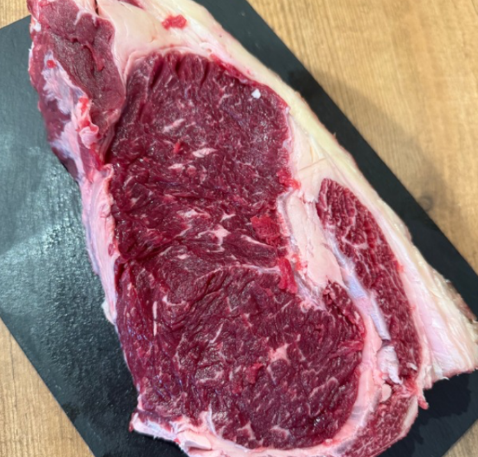 Carne de chuletón de buey cruda, presentada en una tabla negra.