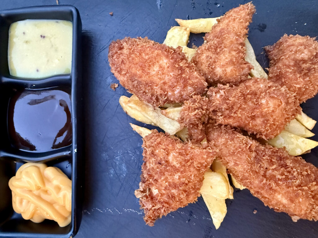 Solomillos de pollo con patatas fritas y salsas variadas en restaurante – Agencia Brilla.
