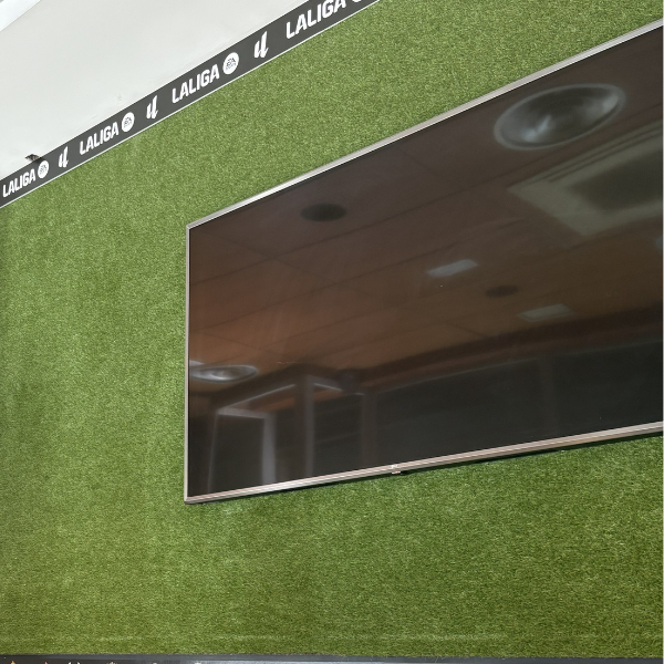 Pantalla de televisión en el bar con decoración de césped artificial y los logos de los equipos de La Liga.